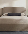 Beige bed with matching headboard in a bedroom setting with two lamps on nightstands.