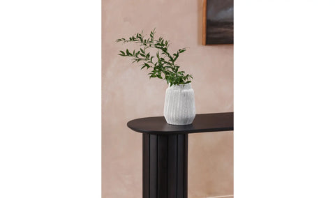 White vase with green plant on a black table against a beige wall