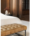 Brown tufted bench in front of a bed with white bedding in a bedroom setting.
